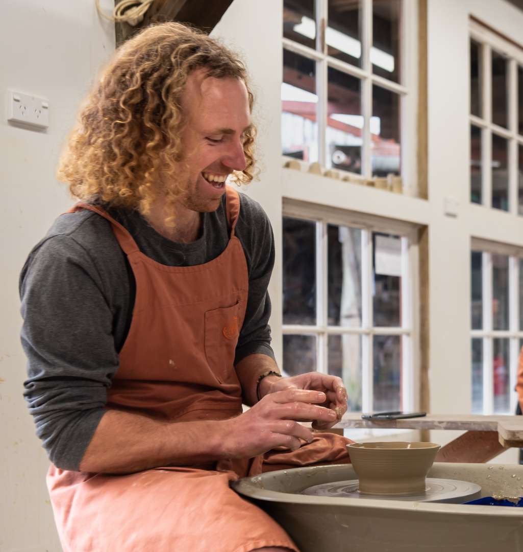 Visitor smiling while creating a bowl on the pottery wheel